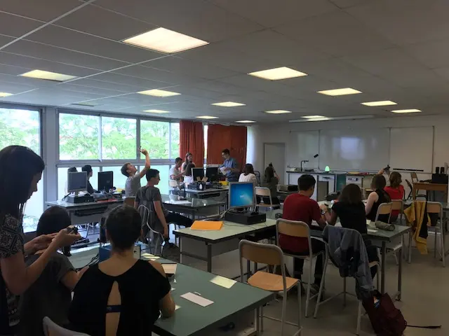 Salle de classe de physique-chimie avec étudiants en activité, utilisation d’ordinateurs et interaction pédagogique.