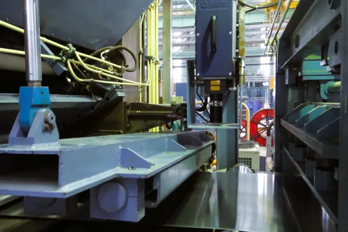 Steel sheet metal passing through laser optical sensor equipment in an industrial metal processing facility for precise length and speed measurement.