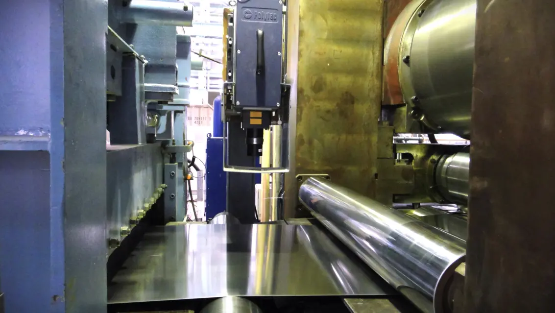 Industrial metal rolling machine processing shiny steel sheet on large rollers inside factory production line