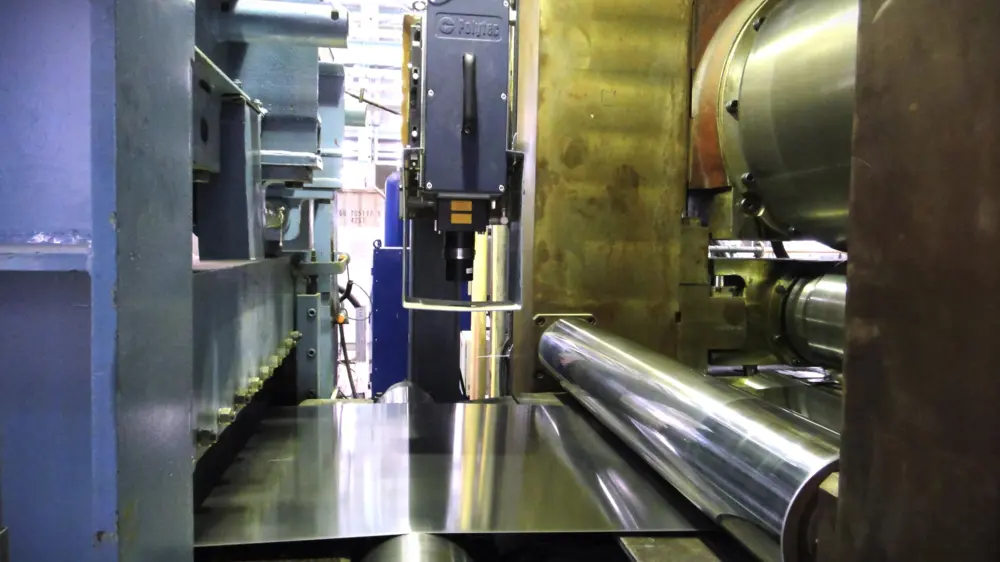 Máquina de laminación en frío controlando el espesor de lámina metálica con sensores ópticos Polytec para flujo másico preciso.